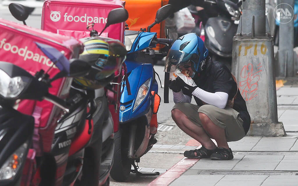 疫情期間許多公司企業改為居家辦公，民眾減少外出，外送需求大增，外送員於送餐空檔蹲在馬路邊吃午餐。